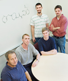 On white board is diagram of the synthetic molecule that signals cell death in cancer cells, identified by Illinois researchers: seated from left, Bill Helferich, professor of nutritional sciences; Paul Hergenrother, professor of chemistry, and Karson Putt, graduate research assistant in chemistry; and standing from left, Joe Sandhorst, graduate research assistant in chemistry, and Martin Hoagland, postdoctoral student in veterinary biosciences.