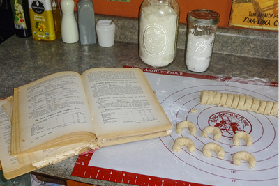 Photo of open cookbook and vanilla crescent cookies being made
