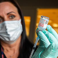 A nurse uses a syringe to draw a dose of vaccine from a vial labeled Moderna.