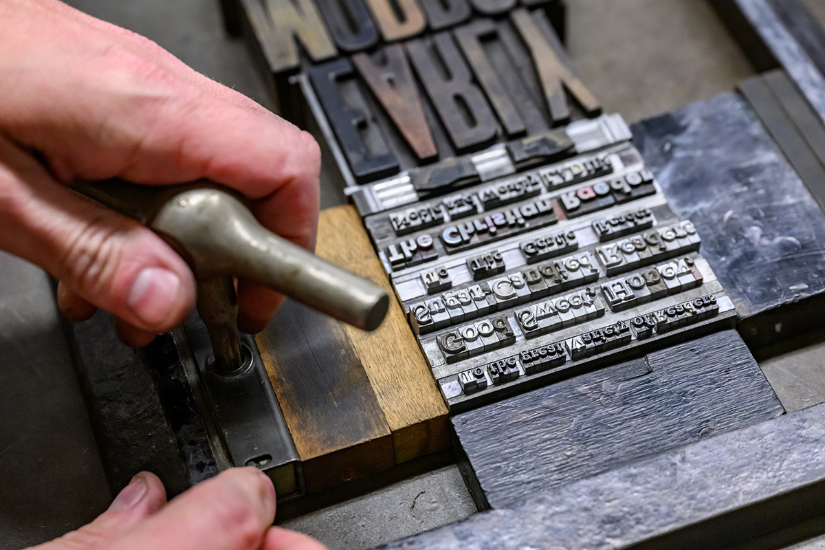 Close-up photo of Ryan Cordell’s hand turning a key in a quoin to exert pressure on a block of type.