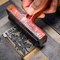 Close-up photo of a roller being rolled across a graphic block to ink it.