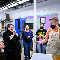 Photo of students smiling and applauding as Ryan Cordell looks at a print he has just taken off a letterpress.