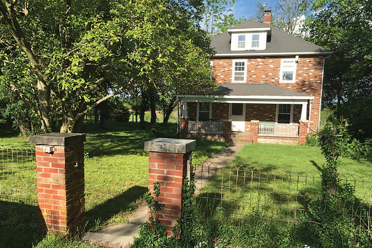 Photo of a brick home surrounded by trees, with brick pillars on either side of the front walk.