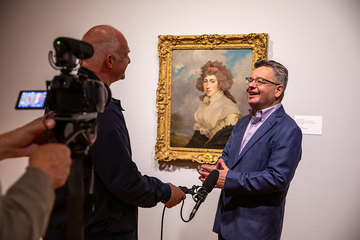 Photo of Craig Koslofsky talking to a man holding a microphone, with a camera man filming and a portrait hanging on a wall behind Koslofsky.