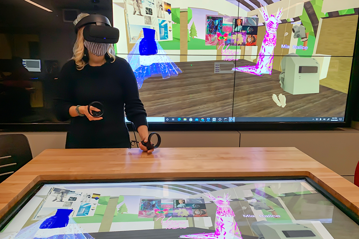 Art professor Chiara Vincenzi wearing virtual reality goggles and standing in front of a screen displaying dresses in a virtual world.