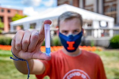 A masked student holds a saliva collection test tube