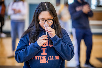 A female student holds a saliva collection tube to her mouth.