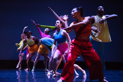 Photo of a group of dancers on stage in colorful clothing.
