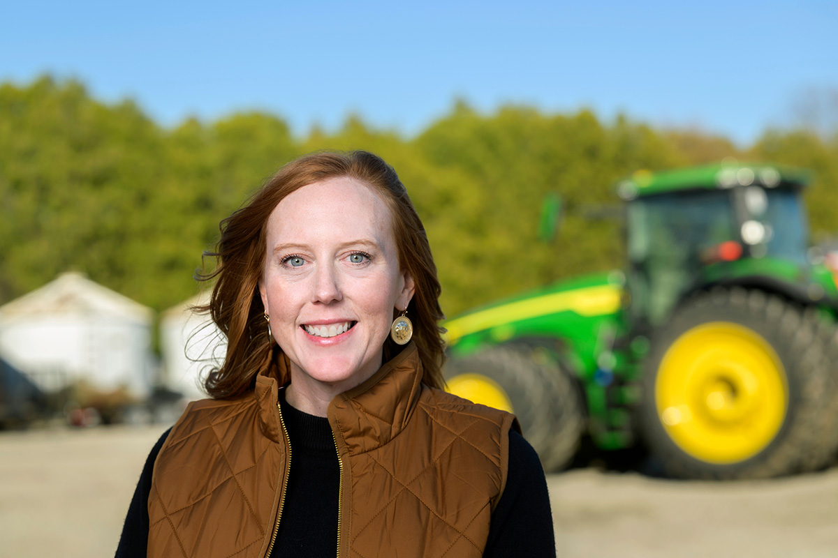 Josie Rudolphi standing outdoors with a tractor in the background on the U. of I. farms