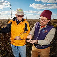Photo of the authors standing together in the prairie. Ellis is holding some seed pods in his hand.