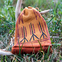 Photo of a deer hide bag decorated with red and black paint sitting in the grass.