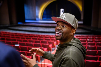 Photo of Tyrone Phillips standing in an empty theater and smiling and gesturing, wearing a White Sox ball cap and a black hoodie.
