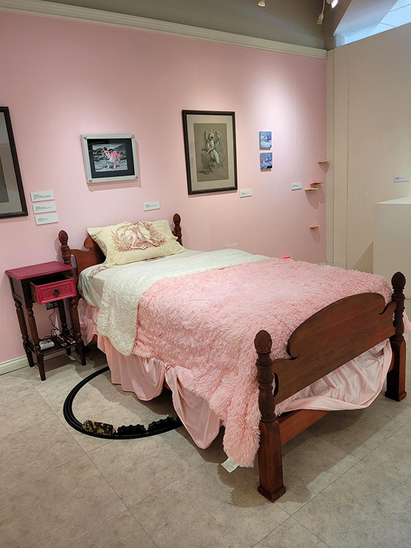 Photo of a bedroom with pink walls and a pink bed comforter, with a toy train coming out from underneath the bed.