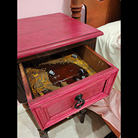 Photo of a nightstand with an open drawer, with a diorama inside the drawer colored brown and yellow with a pool of dark red and some tiny concrete blocks lying around.