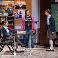 Photo of three young women in a classroom, two of them wearing school uniforms and the third in a t-shirt that says 