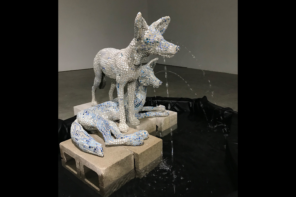 Image of two concrete and glass coyotes next to a fountain and crying water from their eyes.