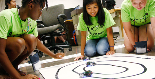 Campers in the robotics camp test small electric cars that they built and programmed. The cars are optically guided, so they are programmed to follow the black lines of tape.