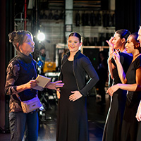 Photo of Elizabeth Auclair talking with dancers in black dresses onstage during a rehearsal break.