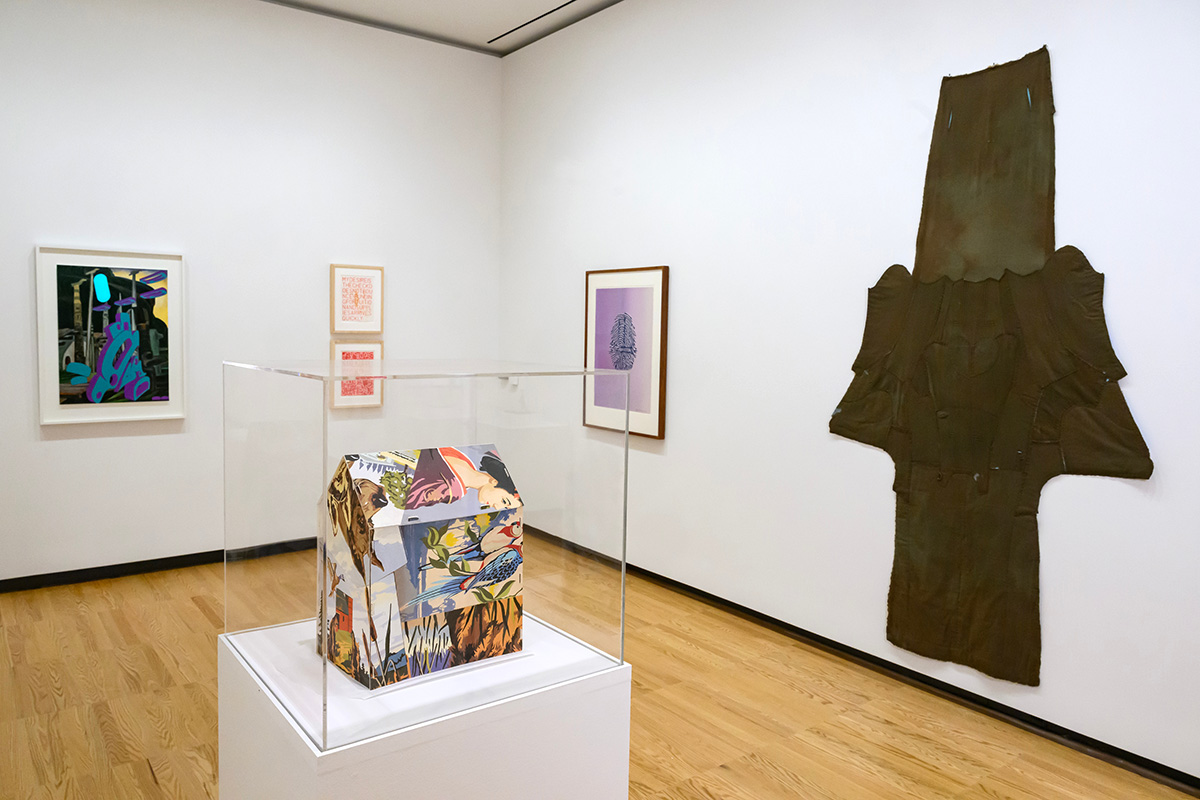 Photo of a gallery at Krannert Art Museum with a fabric wall hanging to the right and a three-dimensional structure covered in prints in the foreground.