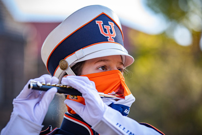 A Marching Illini piccolo player performs while wearing an orange and blue mask with a slit for the mouthpiece of her piccolo.