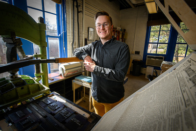Photo of Ryan Cordell leaning on an old hand letterpress in the Skeuomorph Press and Book Lab at the Fab Lab.