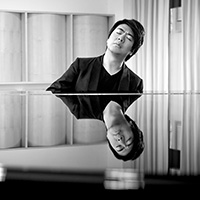 Black and white photograph of a man seated in front of a grand piano, his image reflecting off the surface of the piano.