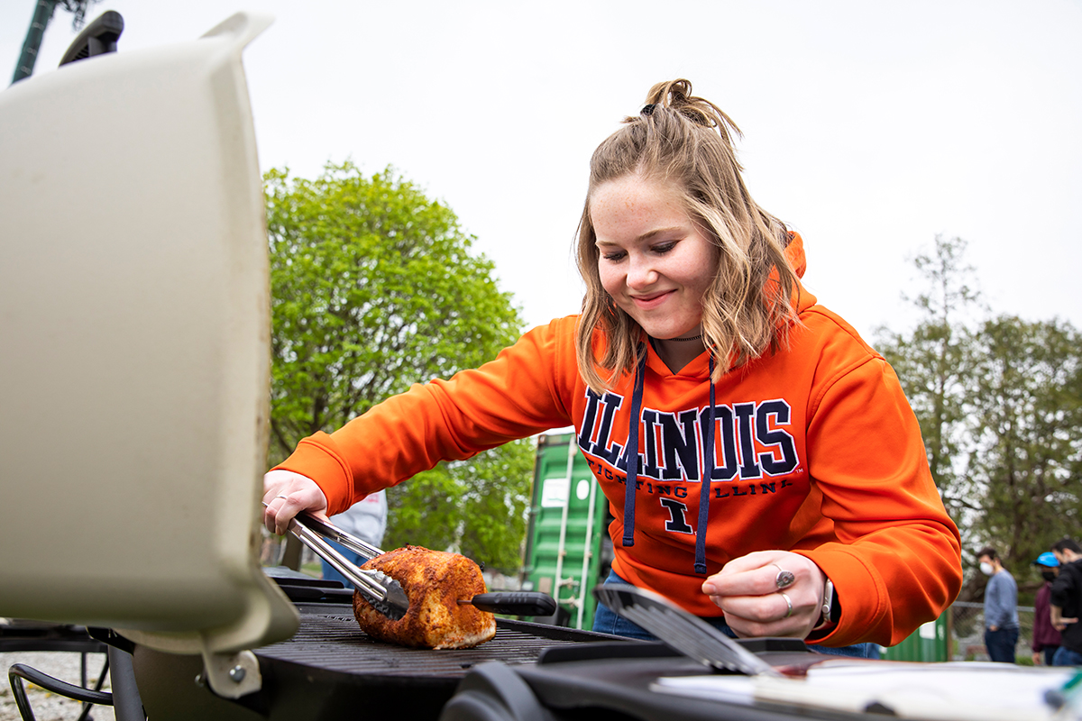 Spangler, wearing an orange U. of I. sweatshirt, smiles as she grasps a pork loin with tongs over a hot grill.