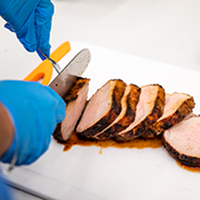 Photo of hands slicing the pork loin on a white surface.