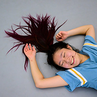 Photo of a dancer lying on the floor with her arms to the sides of her head and her hair from her ponytail spread out above her head.