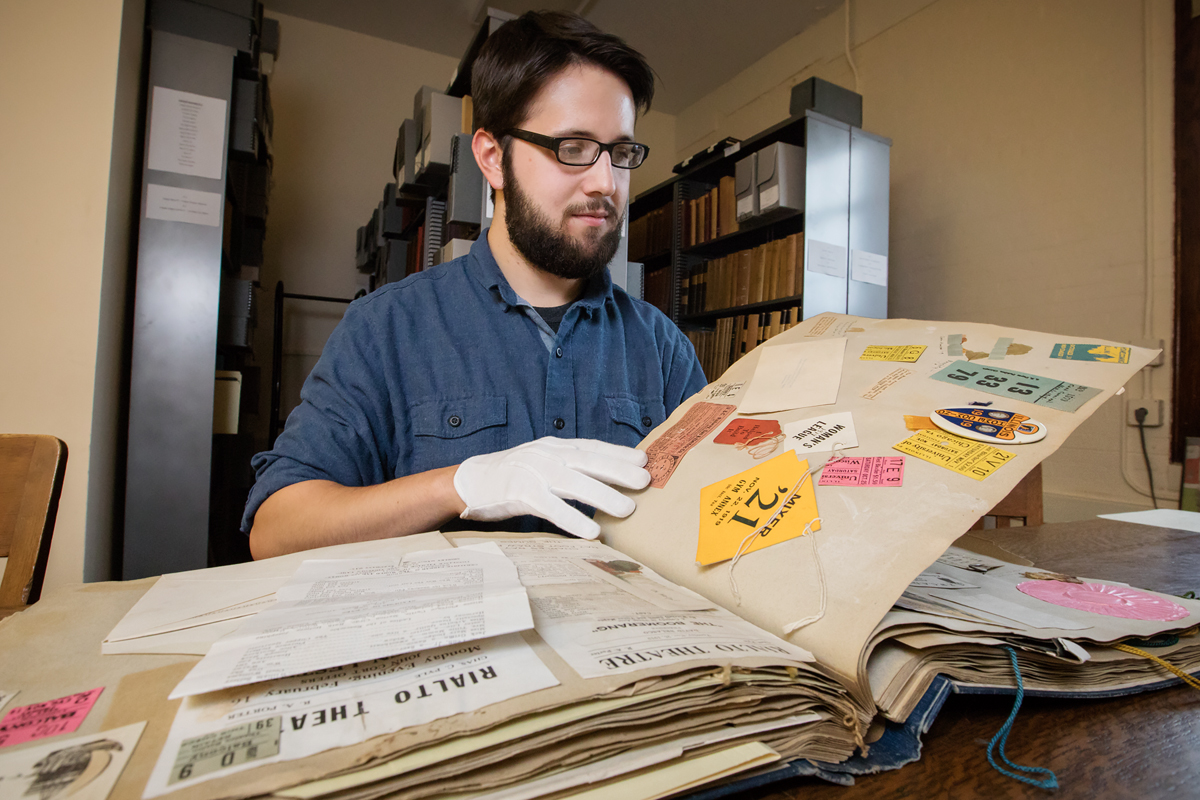 Information sciences graduate student Joseph Porto searches through the scrapbook of a student who attended the university 100 years ago.