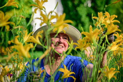Photo of a gardener in a sun hat with yellow flowers in the foreground.