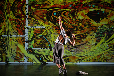 A dancer performs in front a swirling projection of colors
