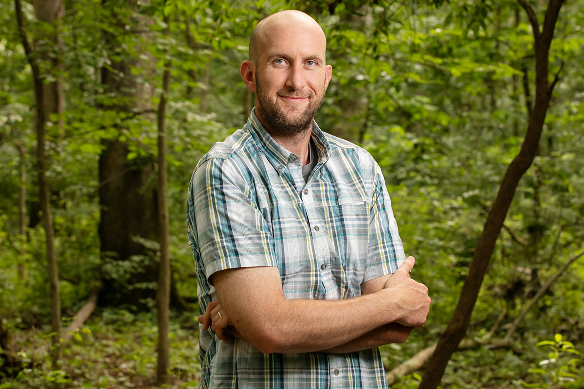 Portrait of researcher standing in the woods with his arms crossed.
