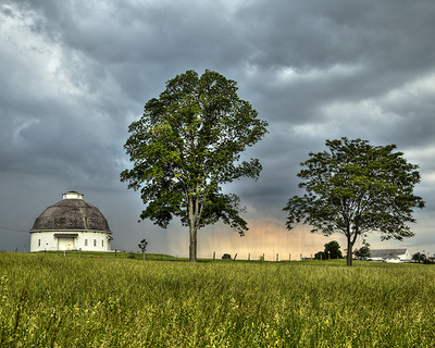 Storm clouds behind a round barn and tree