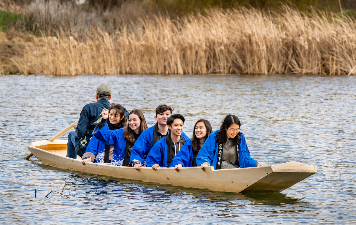 Photo of students floating across a pond in a wooden boat.