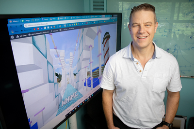 Photo of University of Illinois educational psychology professor H. Chad Lane standing by a screen displaying Minecraft