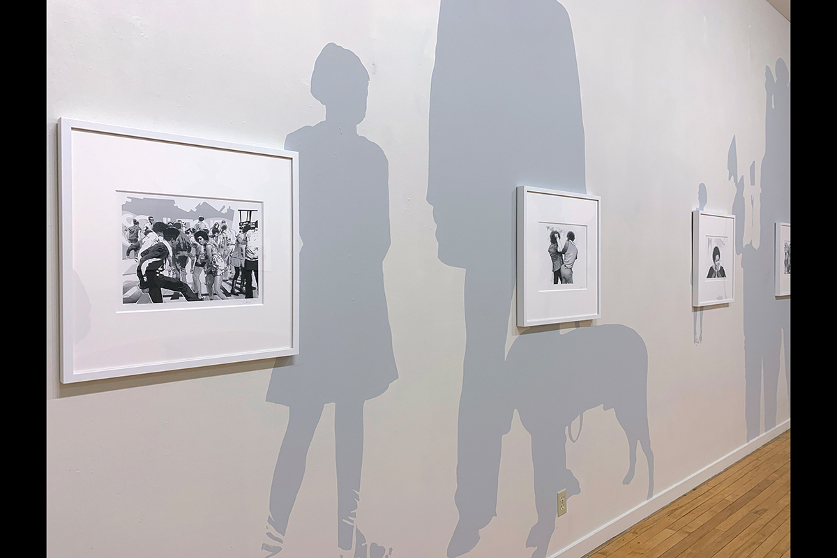 Imgae of a wall painted with light gray silhouettes and displaying framed drawings.