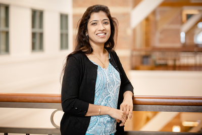 Professor Lavanya Marla stands at the rail of a sunlit atrium overlook in a campus building.