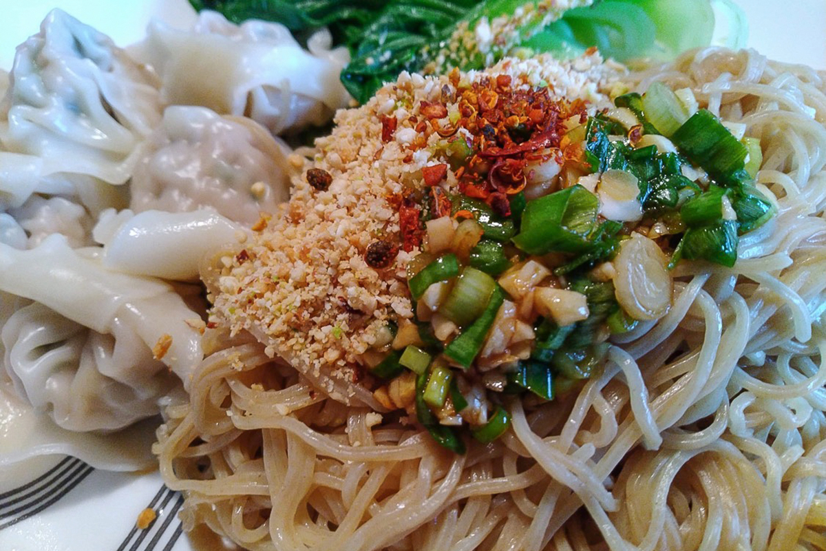A heap of thick noodles is topped with a pile of crushed peanuts, scallions and red chili.