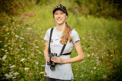 Shelby Lawson stands in a grassy area with binoculars around her neck.