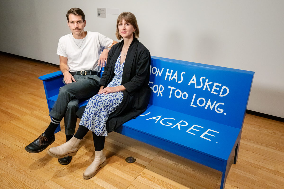 Photo of Christopher Robert Jones and Liza Sylvestre sitting on a bench in an art gallery.