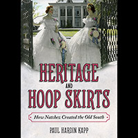 Book cover for “Heritage and Hoop Skirts: How Natchez Created the Old South” showing two Southern belles in hoop skirts in front of a large home.