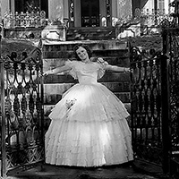 Image of a Southern belle in a hoop skirt on front of a large home.